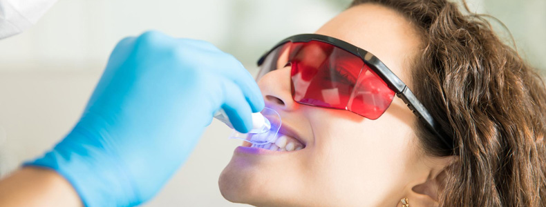 Gülüş Tasarımı, Hollywood Smile (Gülüş Estetiği) tedavisini yapar eli mavi eldiven ile kırmızı gözlüklü hastaya.